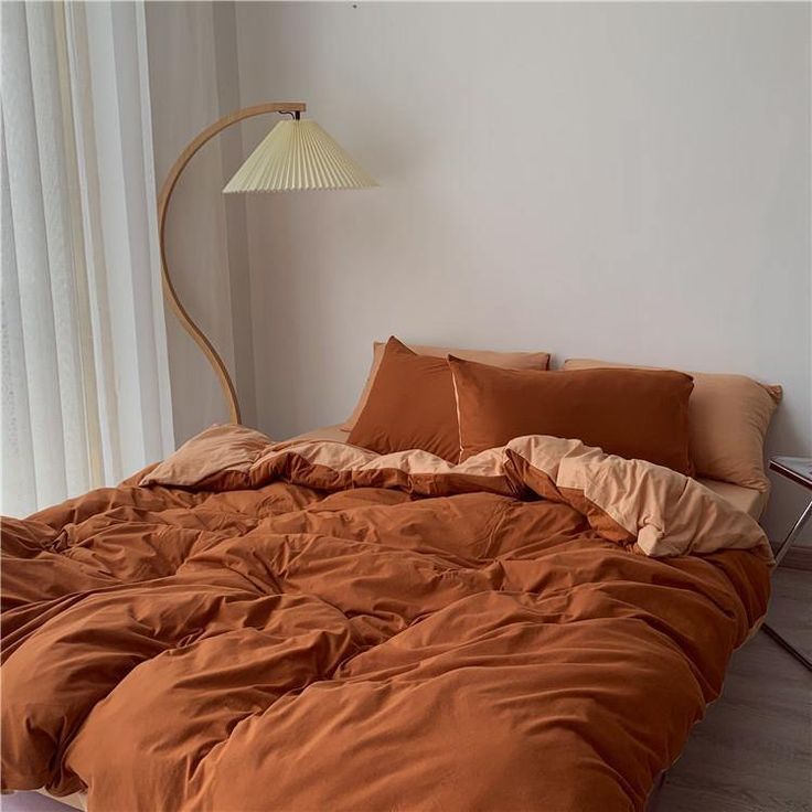 a bed with an orange comforter and two lamps on either side of the bed