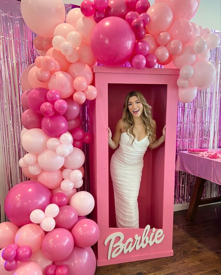 a woman is posing in a barbie photo booth surrounded by balloons