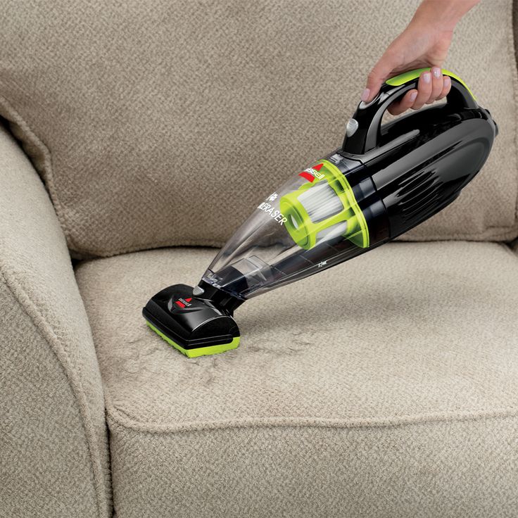 a person using a vacuum to clean a couch