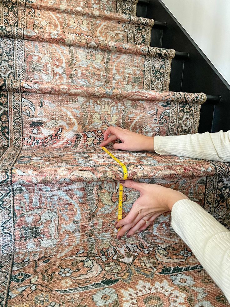 a woman measuring the length of a carpeted stair case with a tape on it