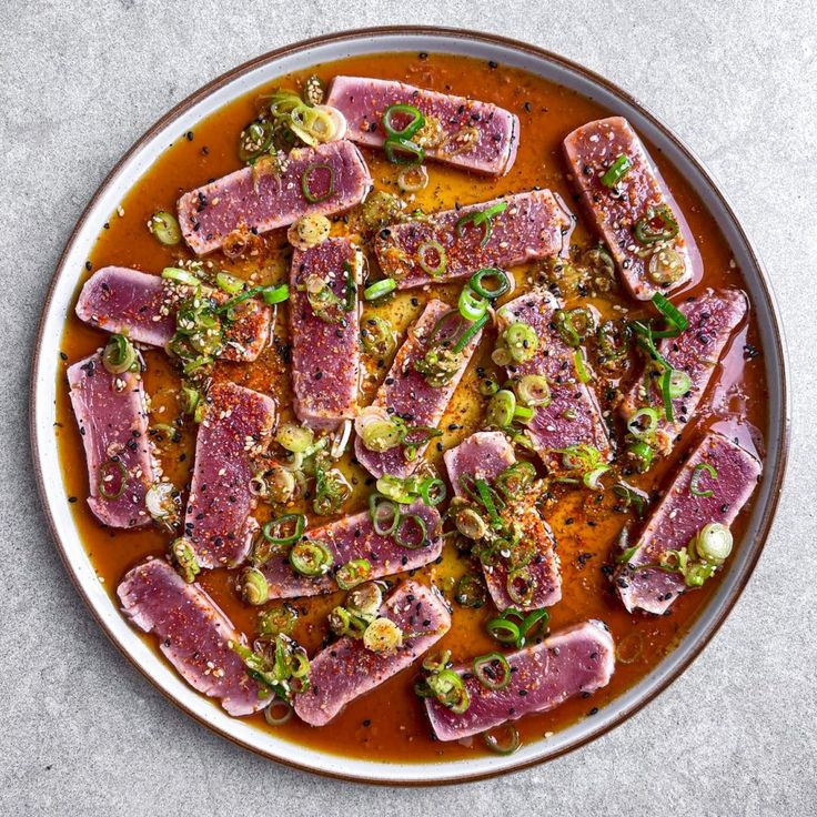 a plate filled with meat and vegetables on top of a white tablecloth next to a spoon