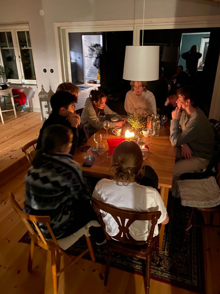 a group of people sitting around a table with candles in the middle and one person standing up