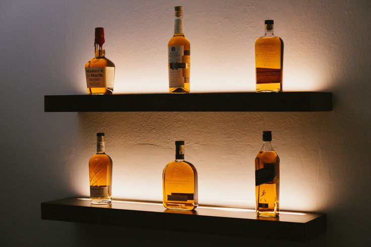 several bottles of whiskey are on shelves lit up by the light coming from behind them