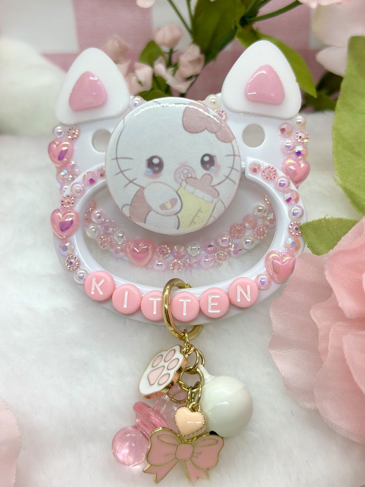 a hello kitty keychain is shown on a white surface with pink flowers in the background