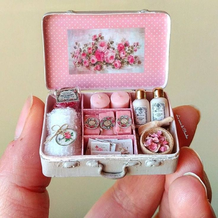 someone is holding a miniature box with items in it and there are pink flowers on the inside