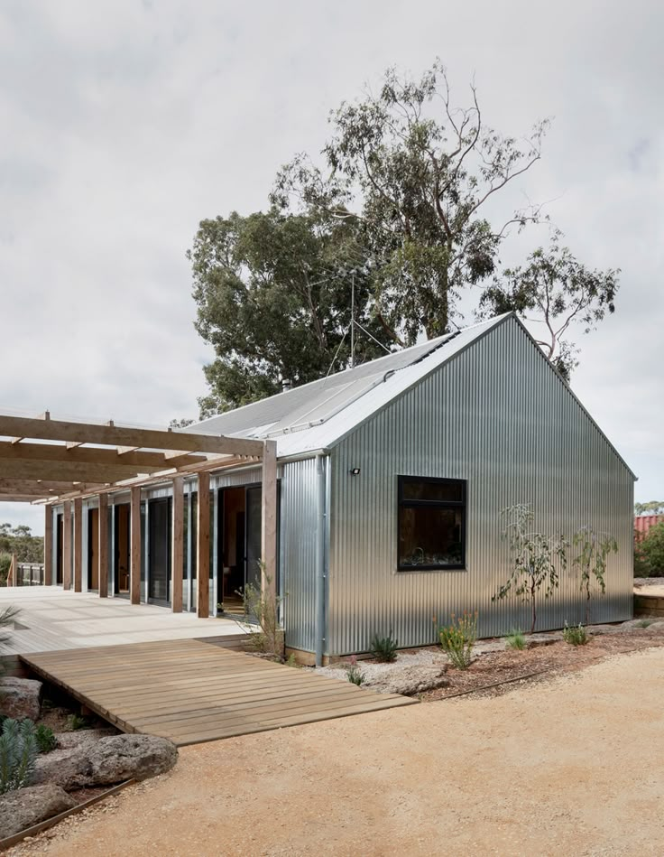 a metal building sitting on top of a dirt field next to a wooden walkway and trees