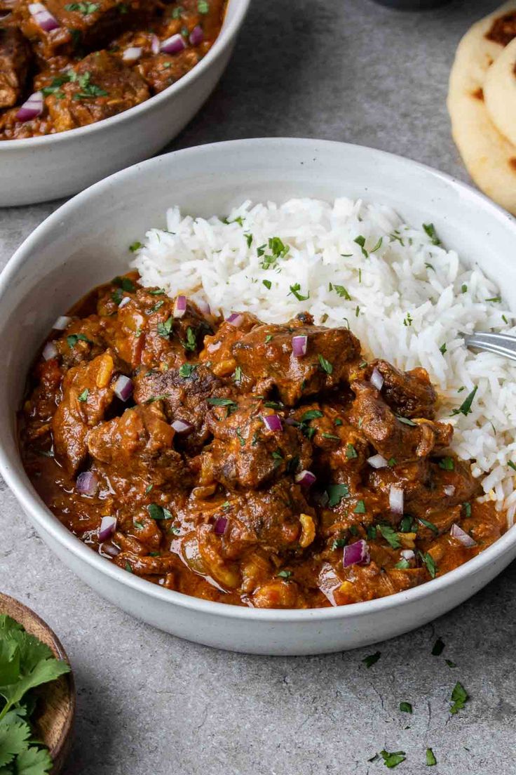 two bowls filled with rice and meat curry next to pita bread on the side