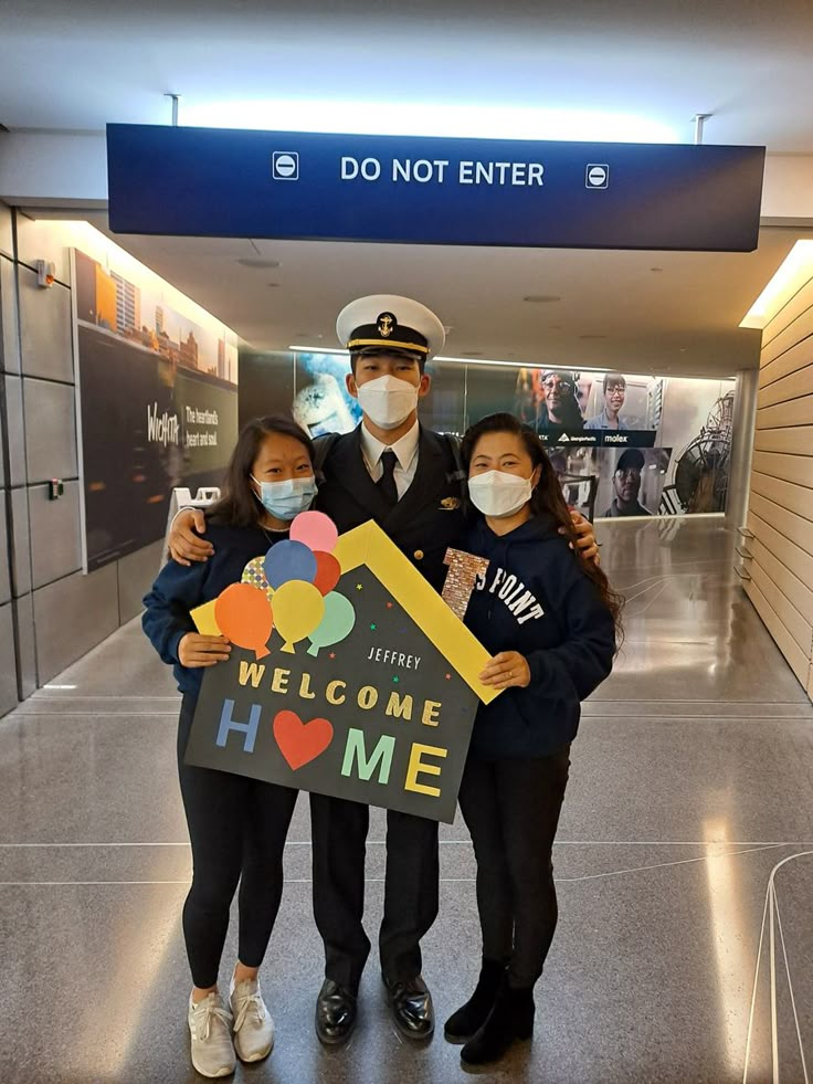 three people wearing masks and holding a welcome home sign in an airport lobby with the words do not enter