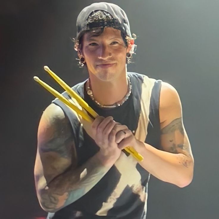 a young man holding two yellow sticks in his right hand and wearing a baseball cap