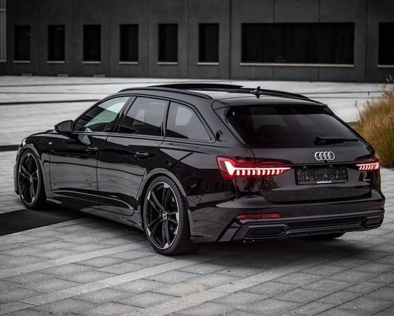 the rear end of an audi car parked in front of a building with its lights on