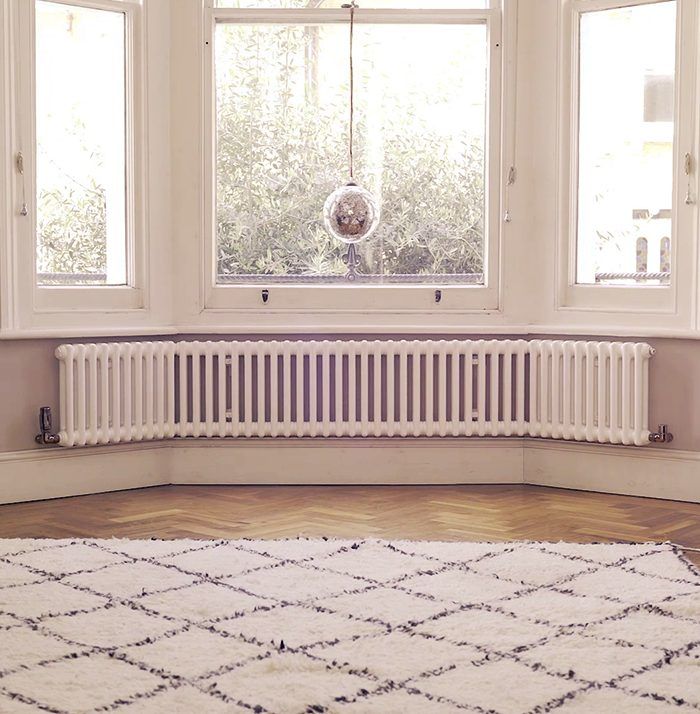 a white radiator sitting in front of two windows next to a rug on the floor