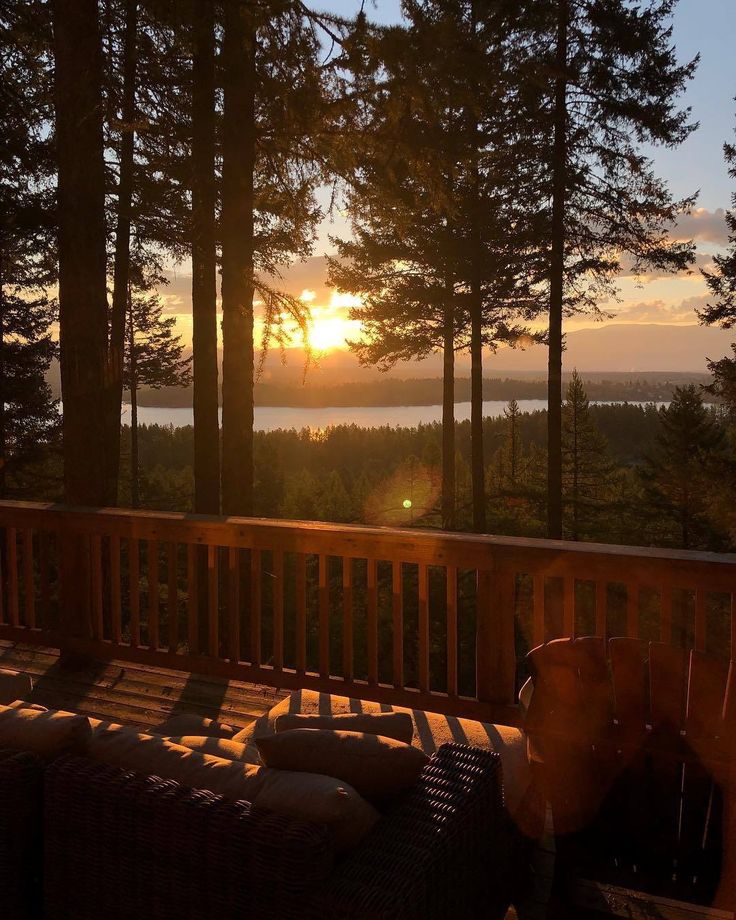 the sun is setting over some trees on a deck with wicker chairs and pillows