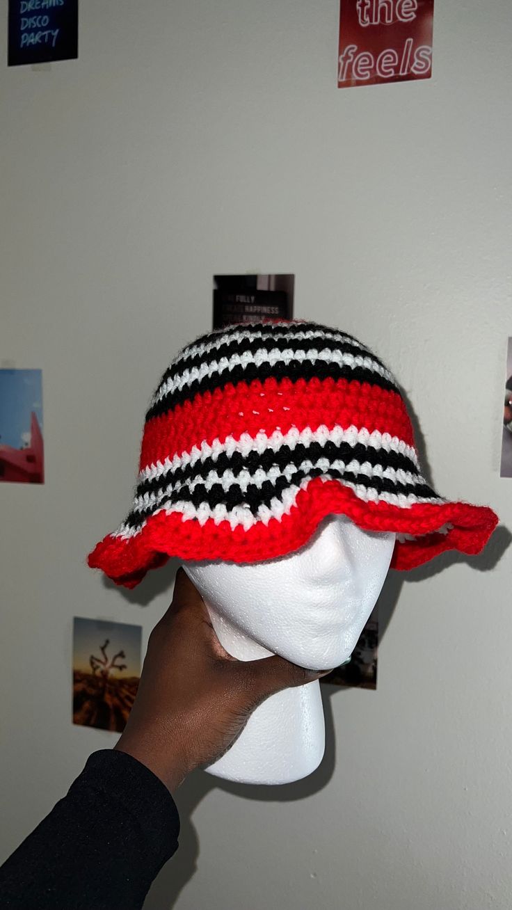 a hand is holding up a red and black hat on a mannequin head