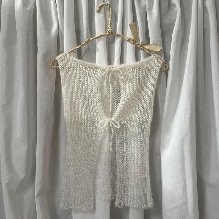 a white sweater hanging on a clothes hanger in front of drapes with curtains behind it