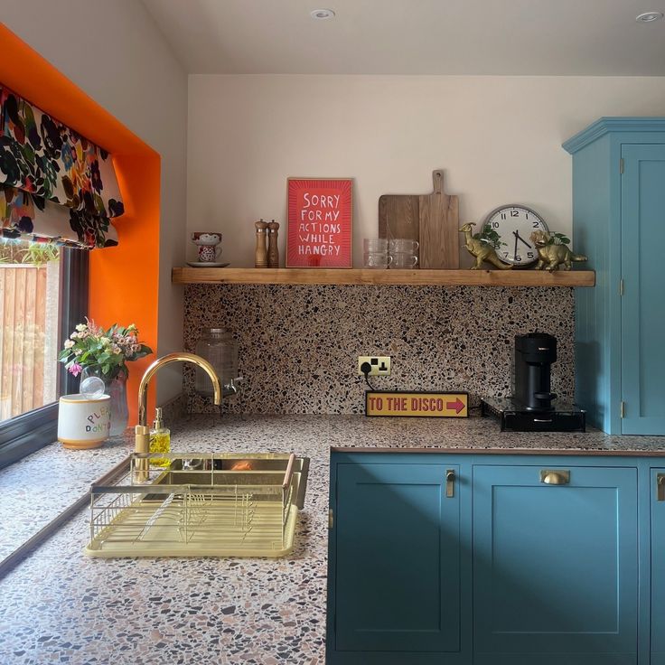 a kitchen with blue cabinets and an orange wall behind the countertop, along with a yellow dishwasher