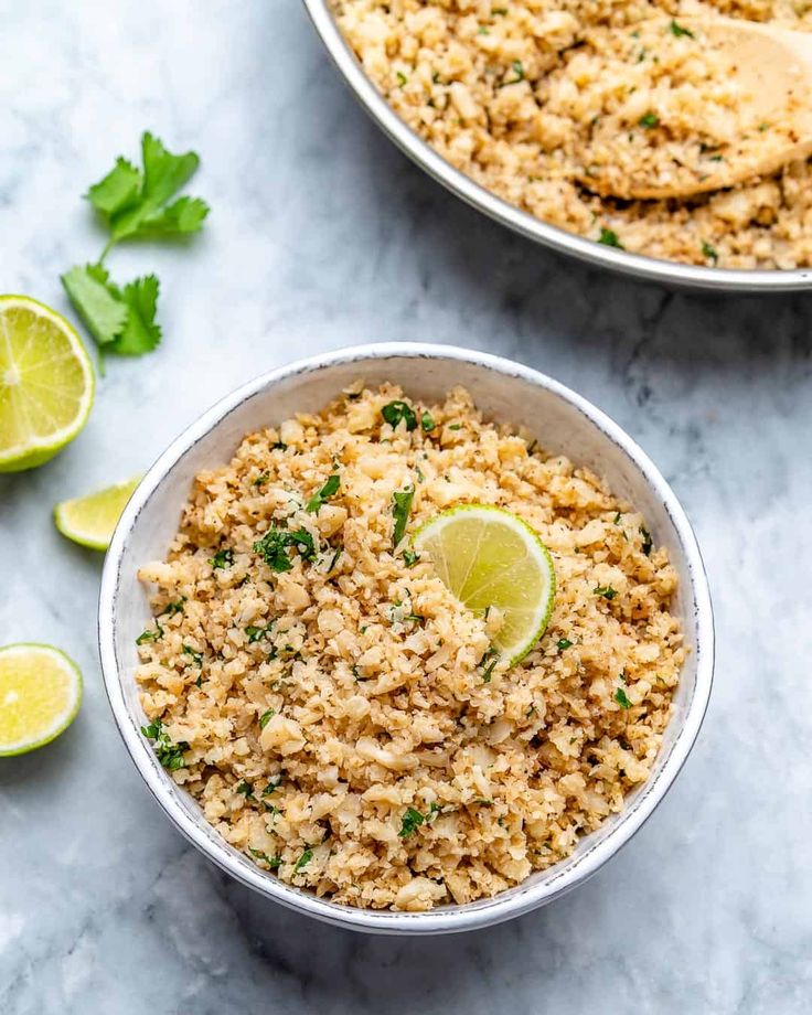 two bowls filled with rice, limes and cilantro on a marble surface