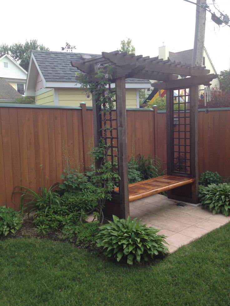 a wooden bench sitting in the middle of a lush green yard next to a fence