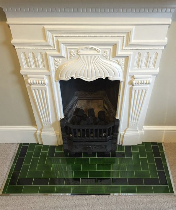 a white fireplace with green tiles and a black fire place in the middle of it