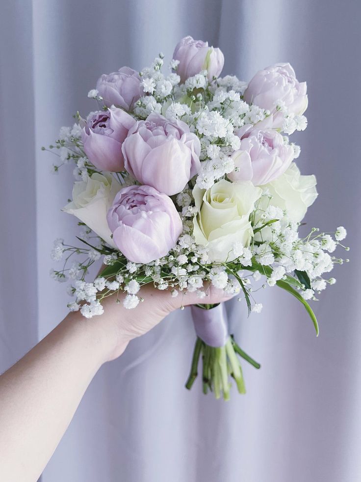 a hand holding a bouquet of white and purple flowers with baby's breath in it