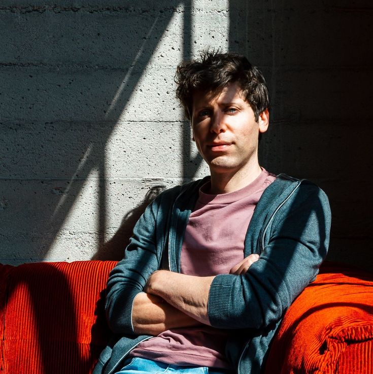 a man sitting on top of a red couch next to a white brick wall with his arms crossed