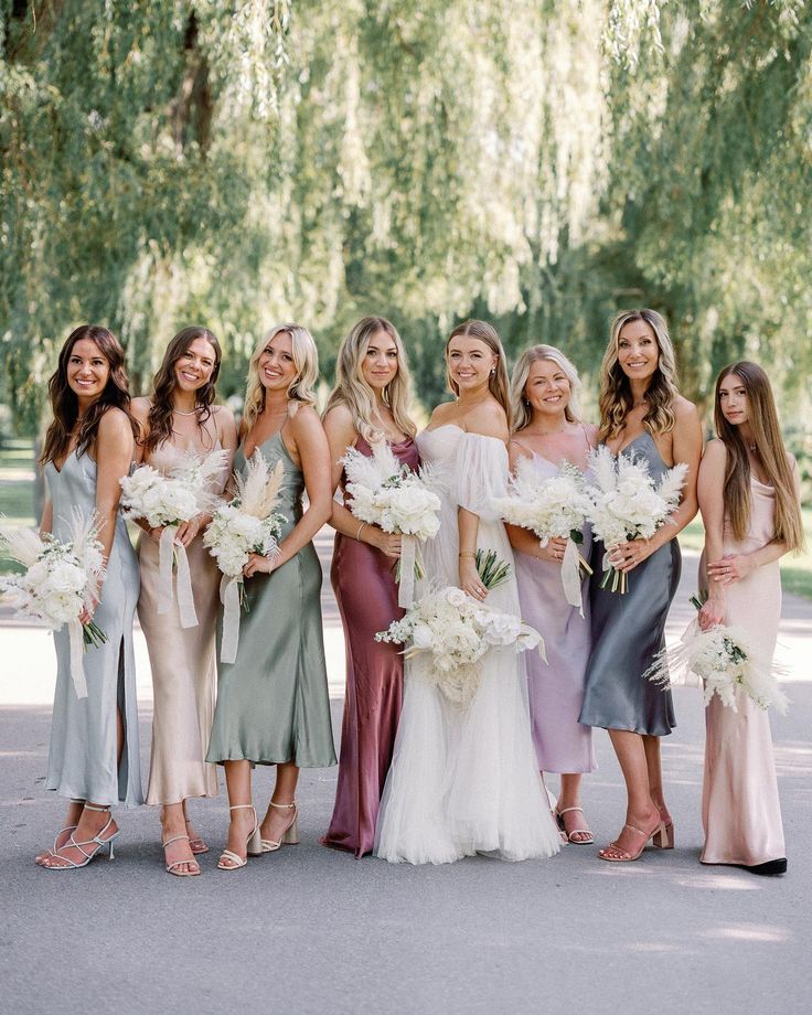 a group of women standing next to each other wearing dresses and holding bouquets in their hands