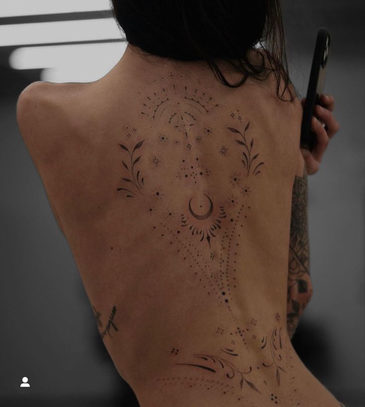 a woman with tattoos on her back holding a cell phone