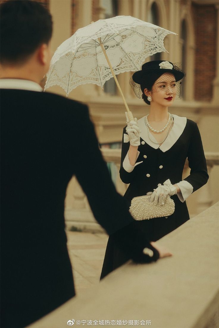 a woman holding an umbrella next to a man in a suit and tie on the street