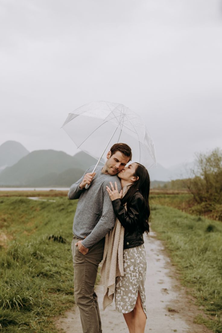 Couple getting cozy in the rain with a clear umbrella while she is kissing him on the cheek. Vancouver Photoshoot, Umbrella Photoshoot, Rainy Photoshoot, Rainy Engagement Photos, Rainy Photos, Rainy Day Photos, Rainy Day Photography, Shooting Couple, Umbrella Photography