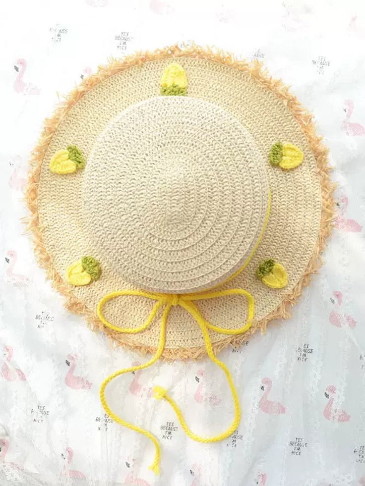 a straw hat with yellow flowers on it laying on top of a white bed sheet