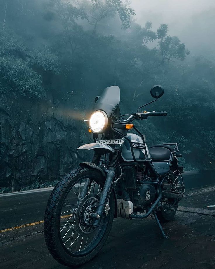 a motorcycle is parked on the side of the road in front of some trees and fog