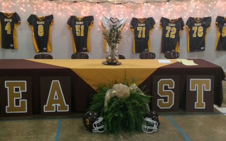 a long table with football jerseys on it and flowers in front of the table is decorated with greenery