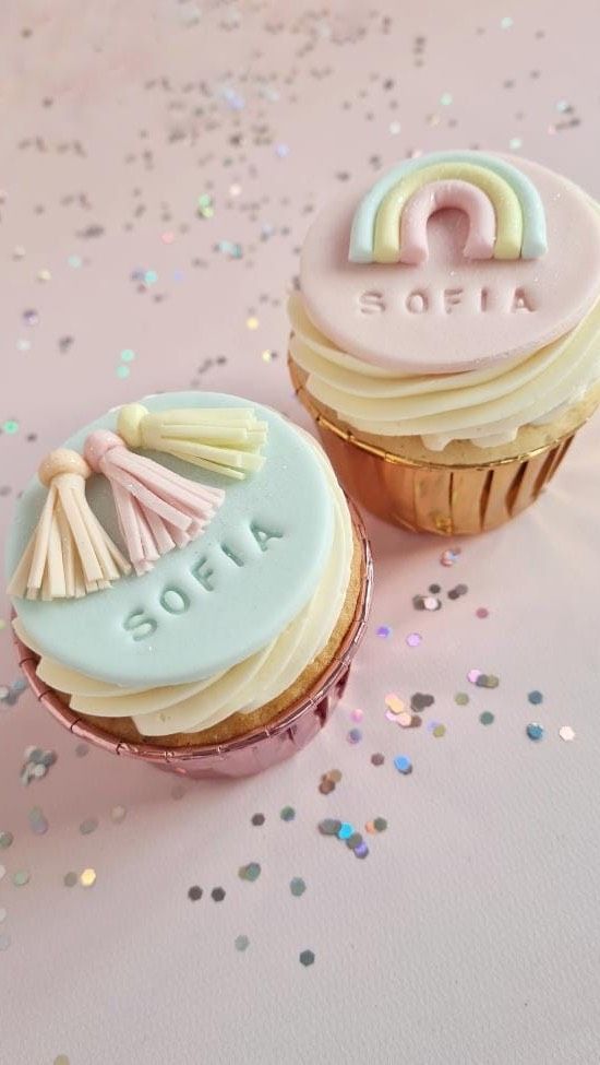 two decorated cupcakes sitting next to each other on top of a pink table