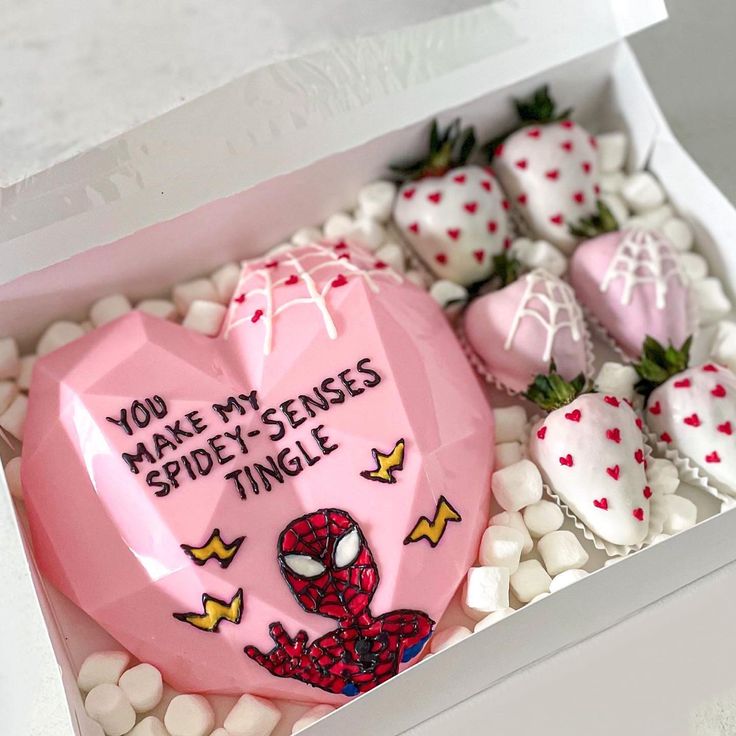 a pink heart shaped box filled with white chocolate covered strawberries and topped with a spiderman design