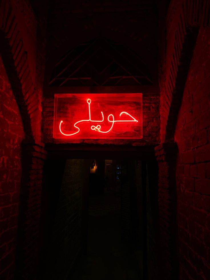 a red neon sign hanging from the side of a brick wall next to a doorway