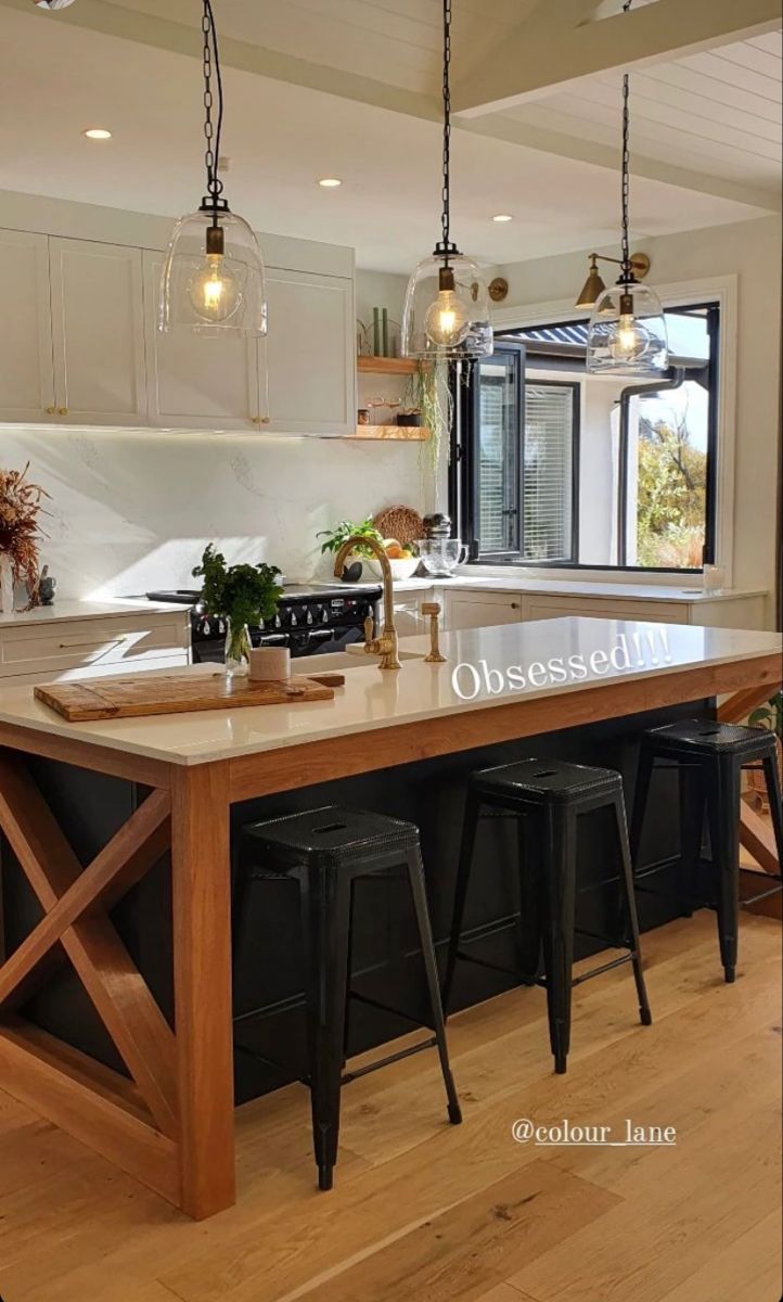 an island in the middle of a kitchen with stools and lights hanging from it