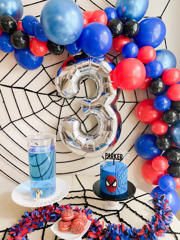 a spiderman birthday party with balloons, streamers and cake on a table in front of the number 3