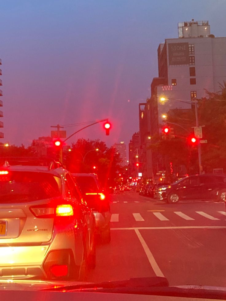 cars stopped at a red light in the city during sunset or sunrise, with buildings and traffic lights behind them