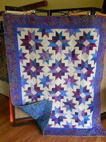 a purple and blue quilt sitting on top of a wooden floor next to a chair