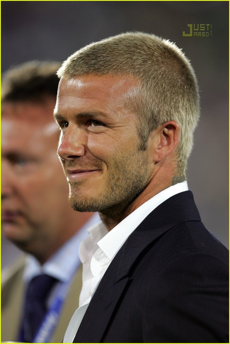 a close up of a person wearing a suit and tie with another man in the background