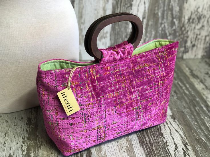 a pink purse with a wooden handle sitting next to a white pillow