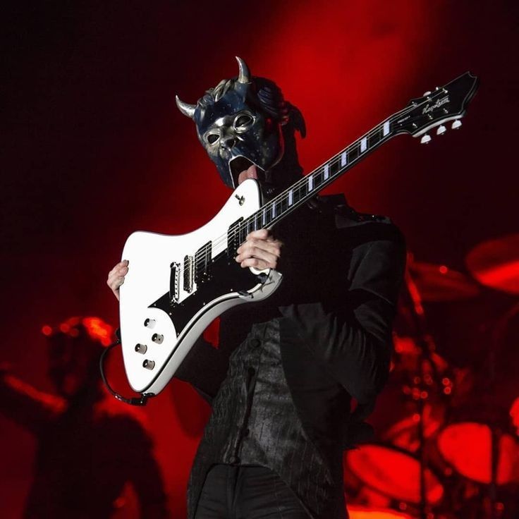 a man wearing a mask and holding a guitar in front of his face on stage