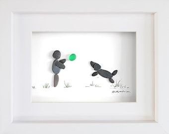 two paper cut figures are in a white frame with grass and rocks on the ground