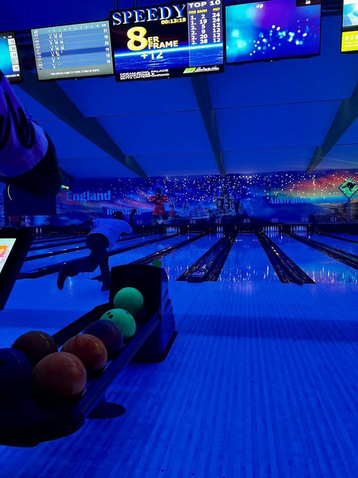 a bowling alley with several lanes full of bowling balls and neon lights in the background