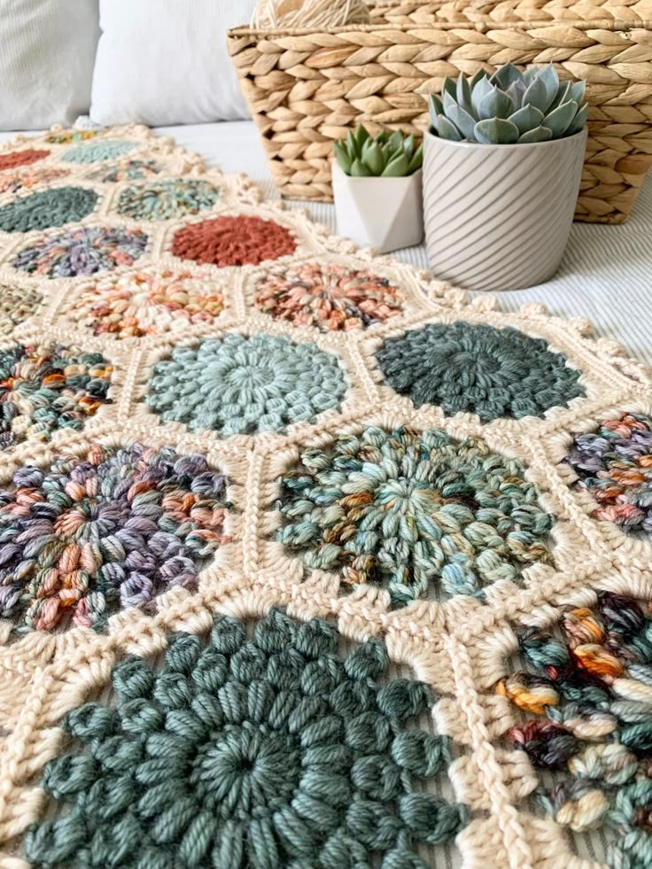 a crocheted blanket on a bed next to a basket with succulents