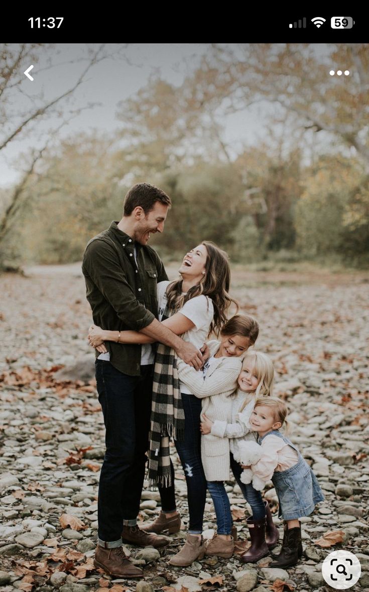 a family standing together in the middle of a field with leaves on the ground and trees behind them