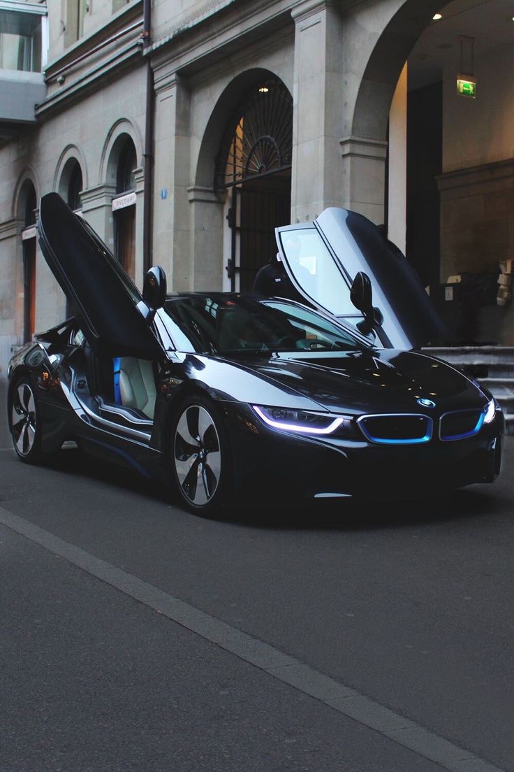 a bmw car with its doors open on the street in front of a large building