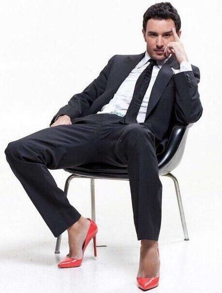 a man in a suit and red shoes sitting on a chair with his feet up