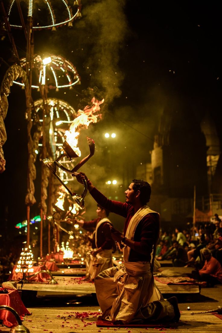 a man sitting on the ground with fire in his hand and people standing around him