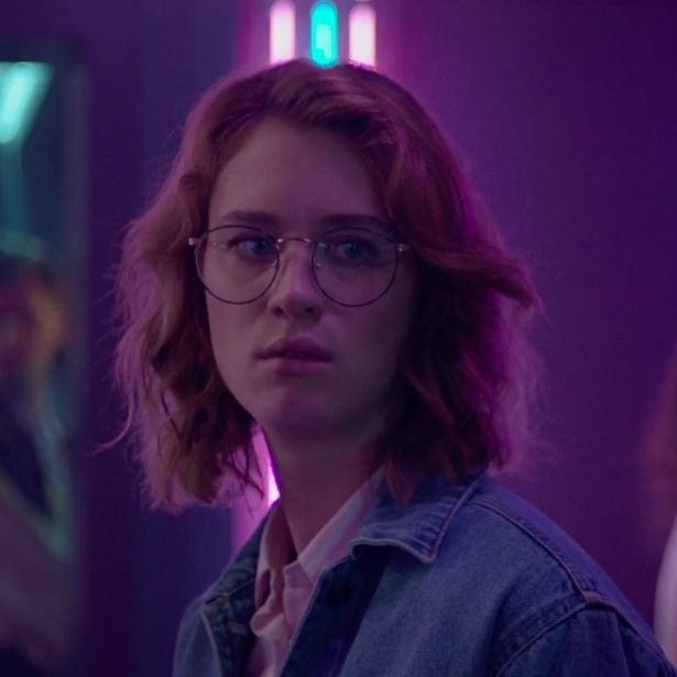 a woman with glasses standing in front of a purple light and looking at the camera