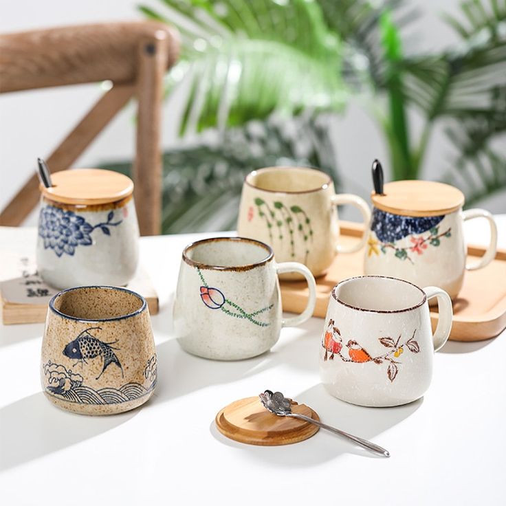 five coffee cups with fish designs on them and spoons next to each other, sitting on a table